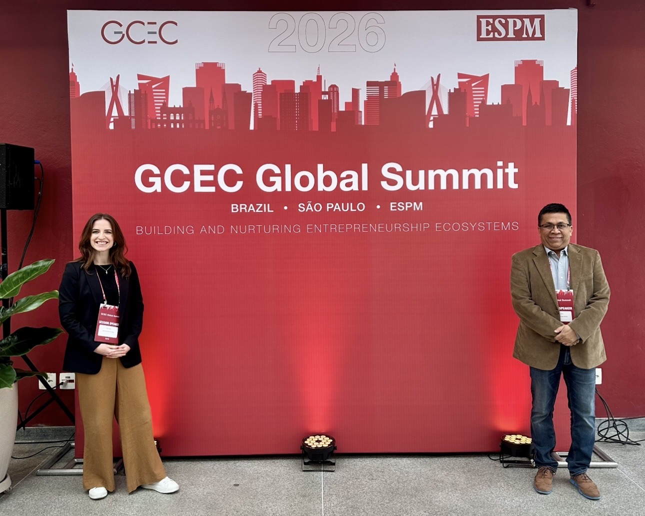 Farah and Mazhar stand in front of the GCEC Global Summit backdrop
